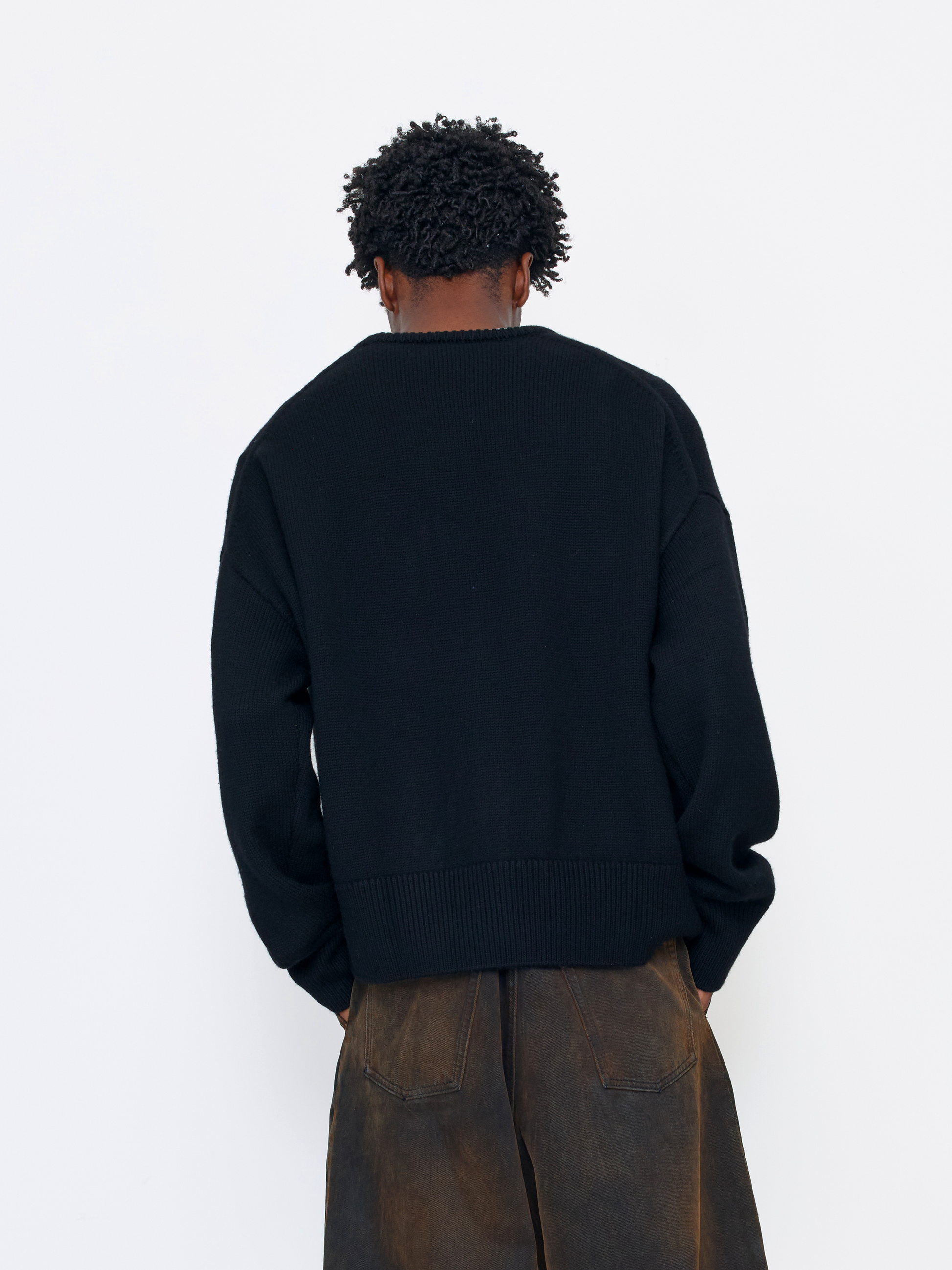 A person shown from the back wearing a black knit sweater and brown wide-leg pants against a plain white studio background.