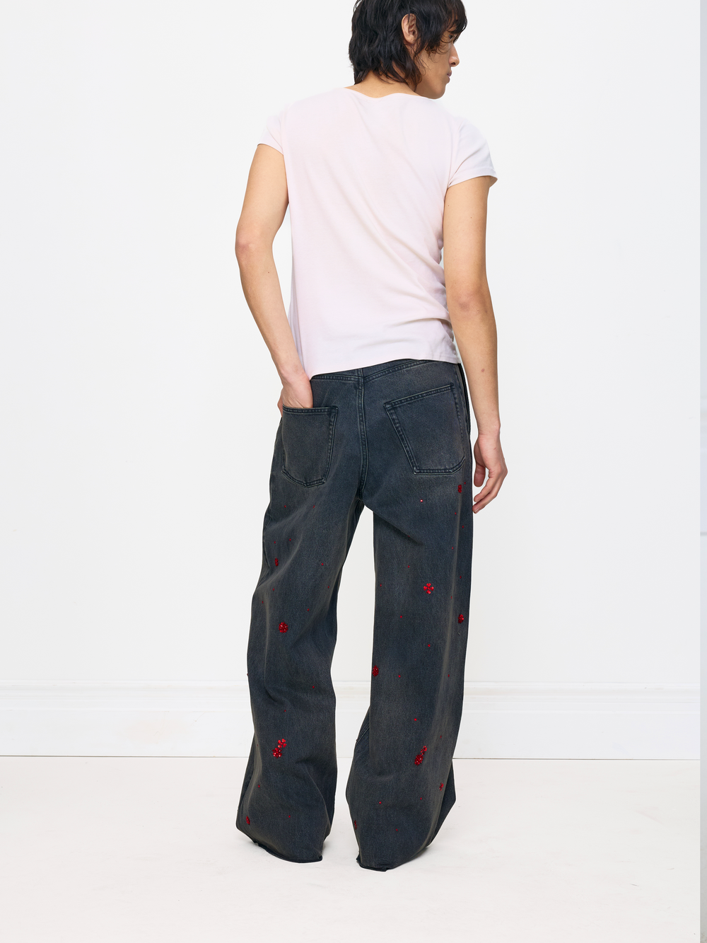 Person wearing dark jeans with red embellishments on a white background