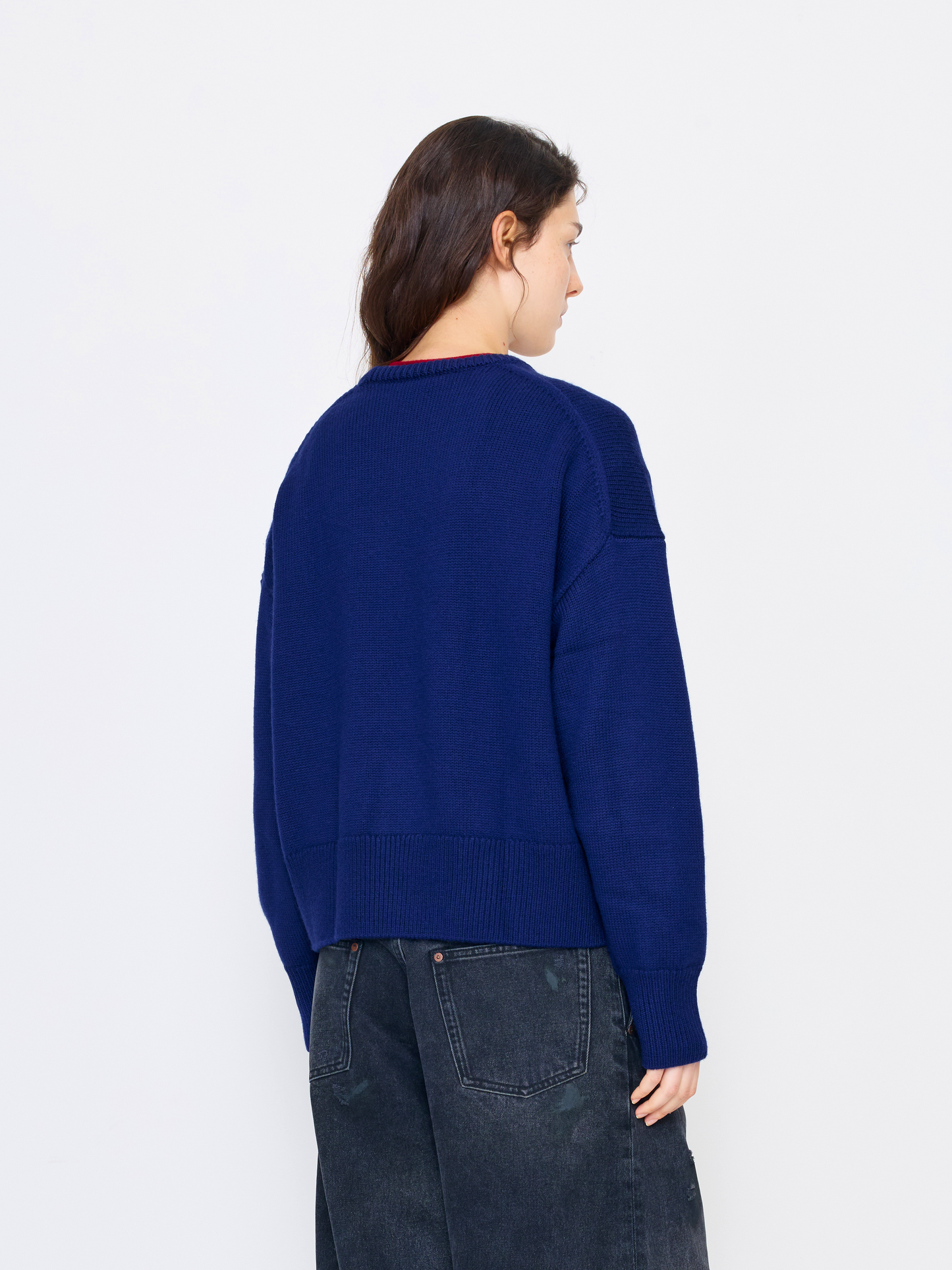 A woman shown from the back wearing a navy blue knit sweater with dark denim jeans, photographed against a clean white studio background.