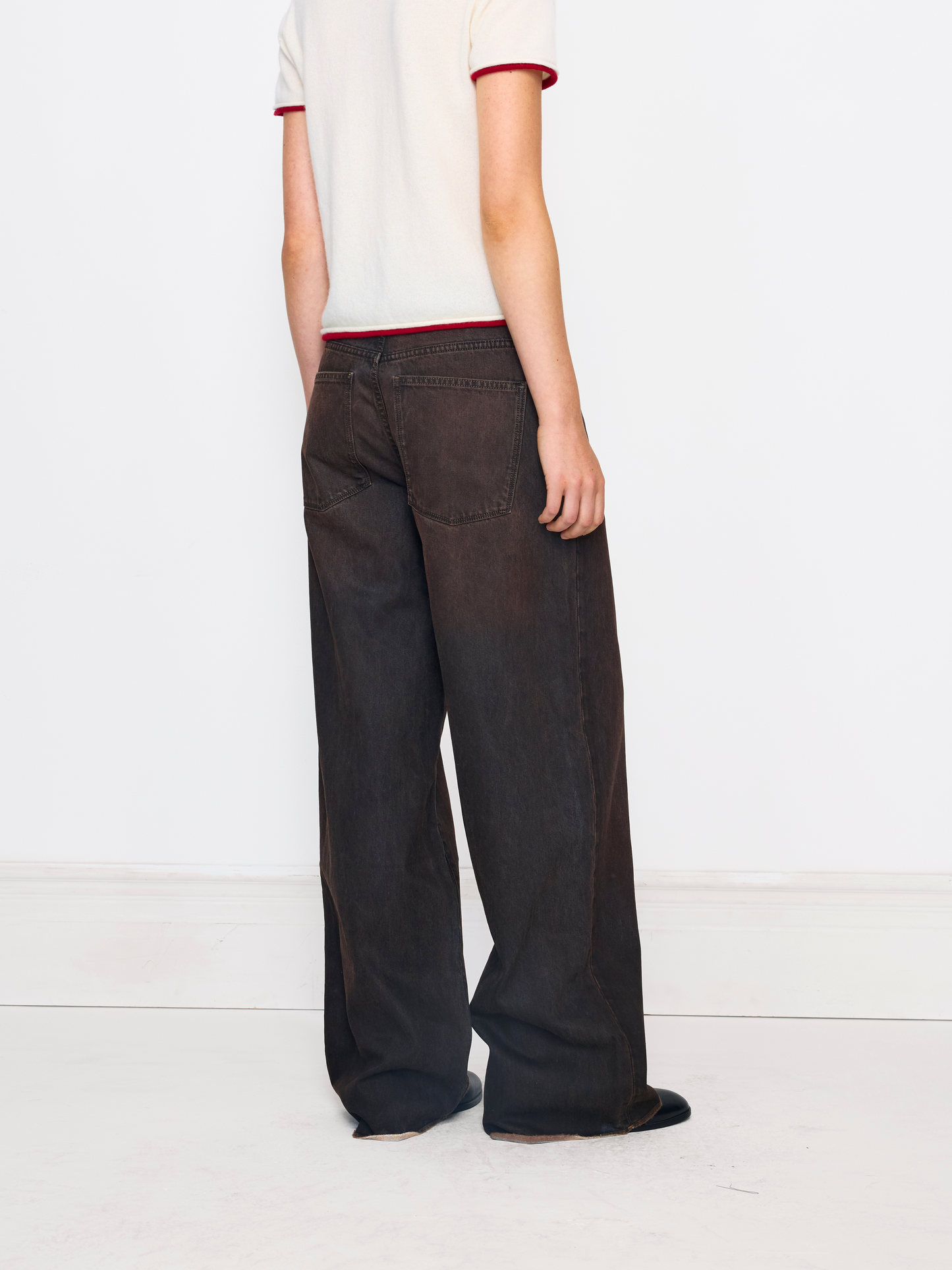 A person shown from the back wearing dark brown wide-leg pants and a white ringer t-shirt with red trim, standing against a plain white studio background.