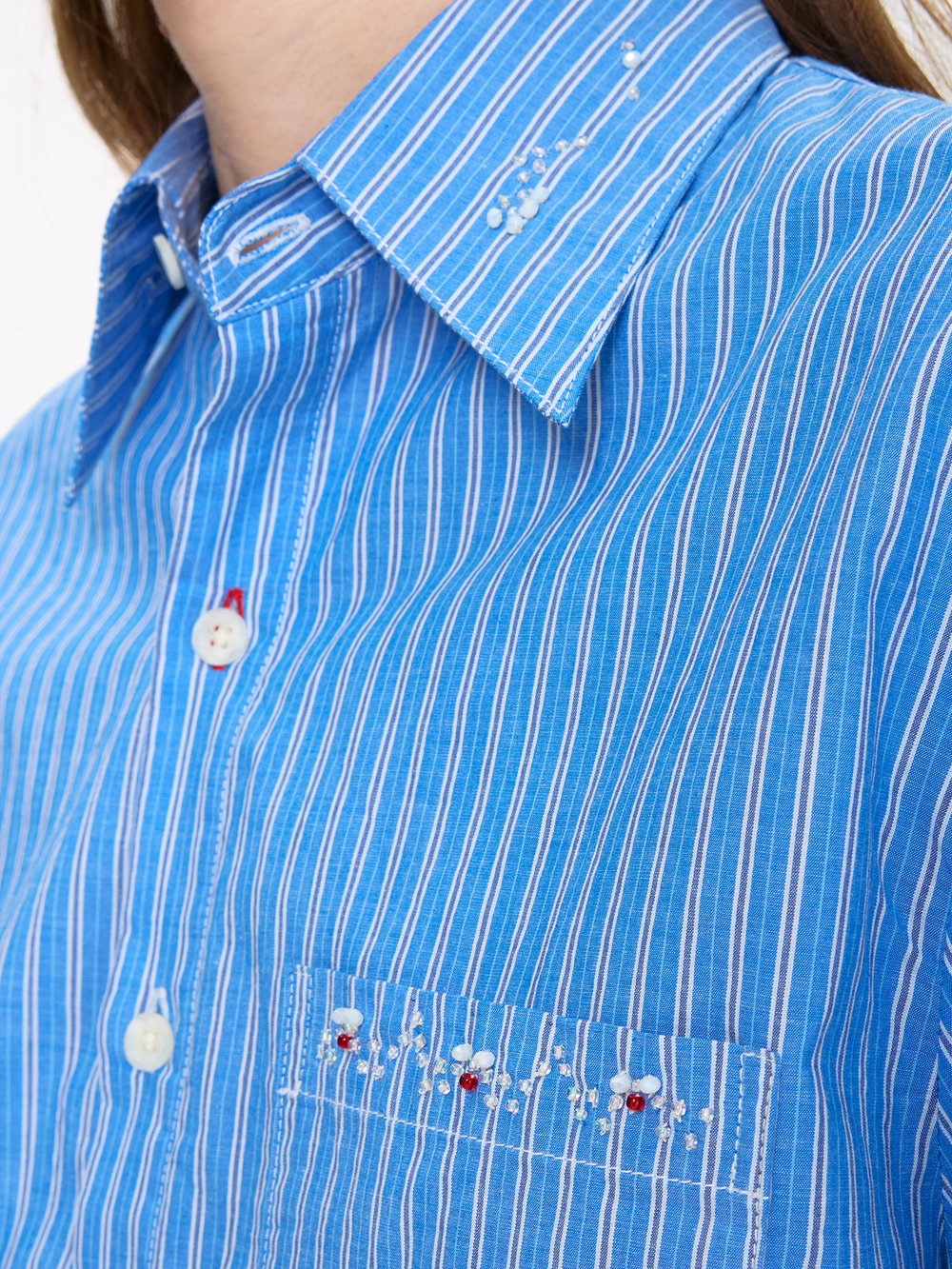 Close-up of a blue striped shirt with white buttons and embroidery on a white background