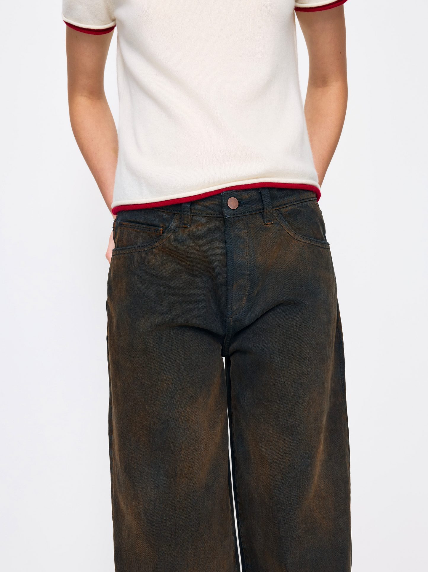 A person wearing dark brown washed wide-leg jeans and a white short-sleeve ringer t-shirt with red trim, shown from the chest down against a light gray studio background.