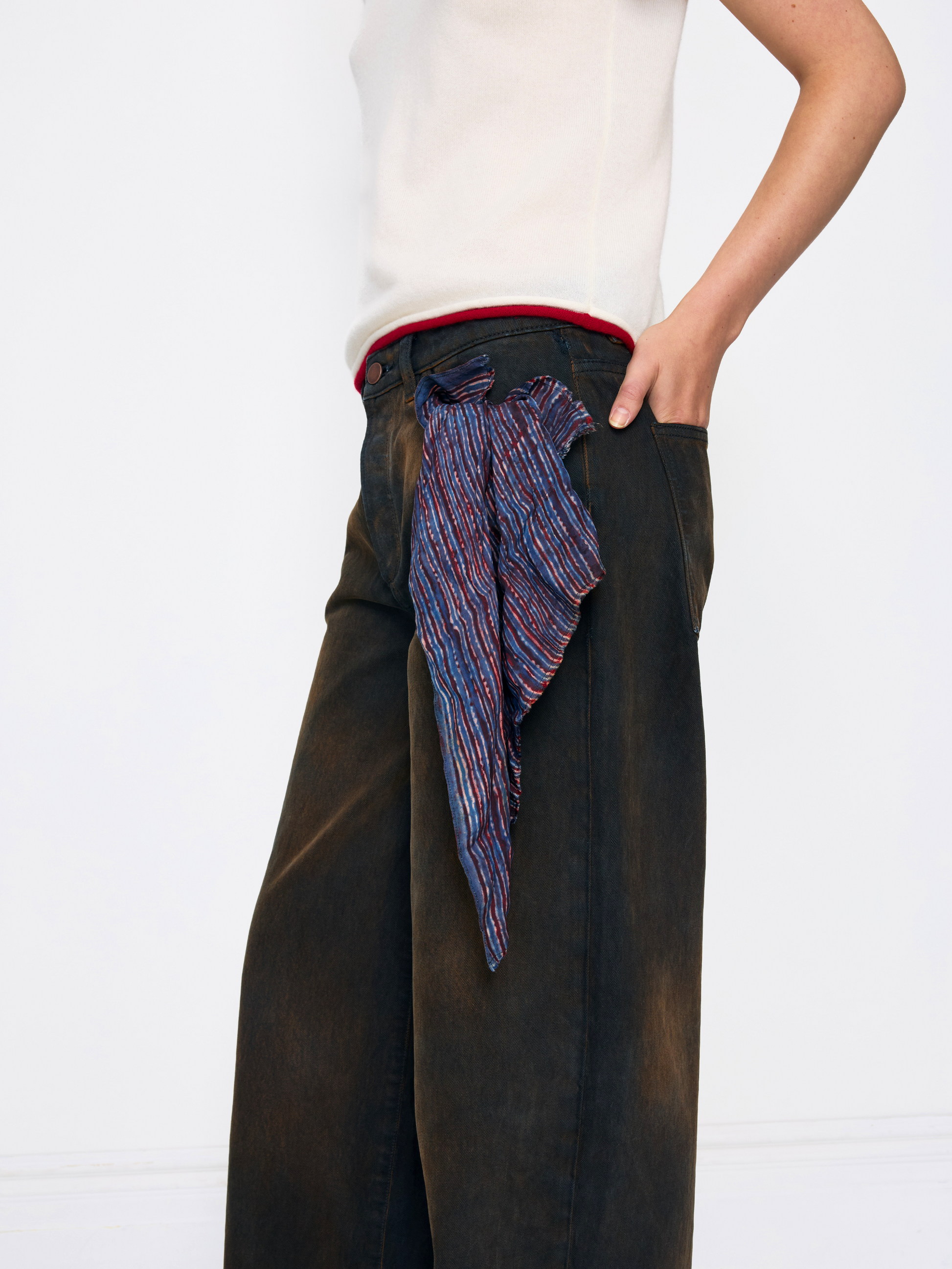 A model wearing dark brown wide-leg trousers with a colorful striped silk scarf tied around the waist, paired with a white top against a white background.