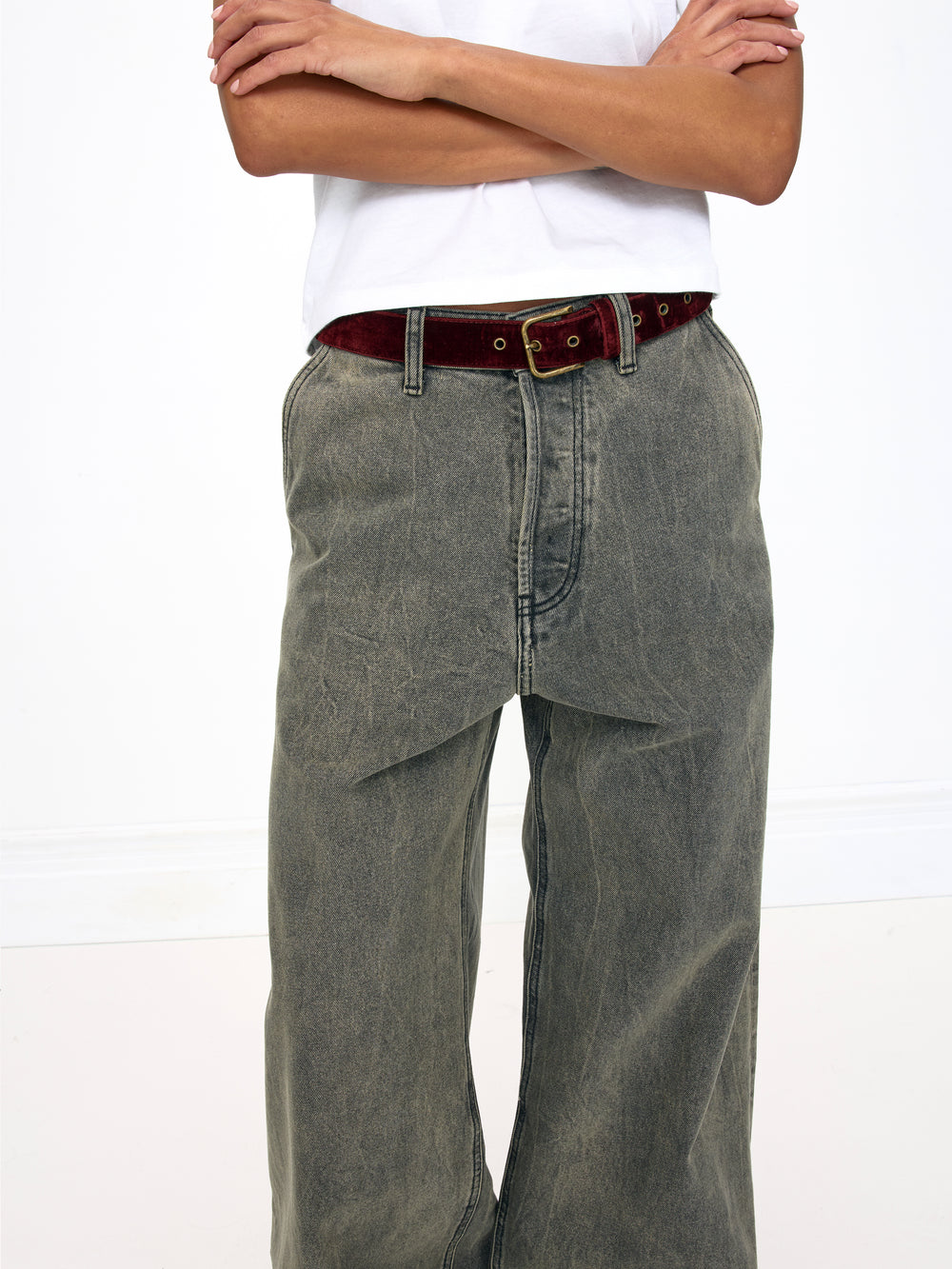 Person wearing gray jeans with a red belt on a white background