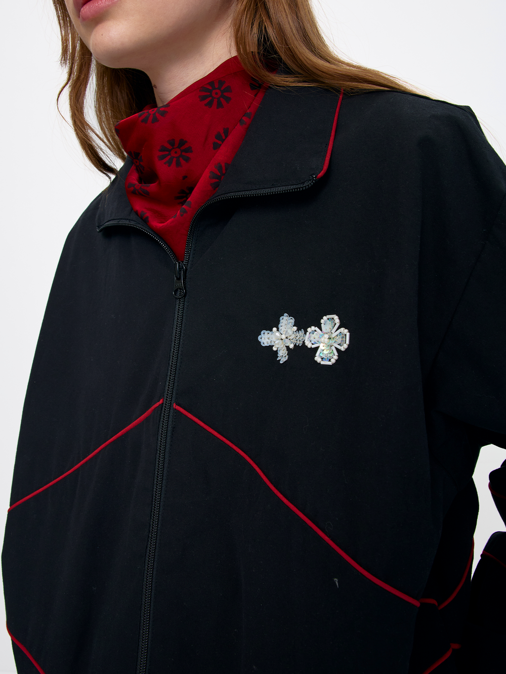 Black jacket with red trim and floral brooches on a white background