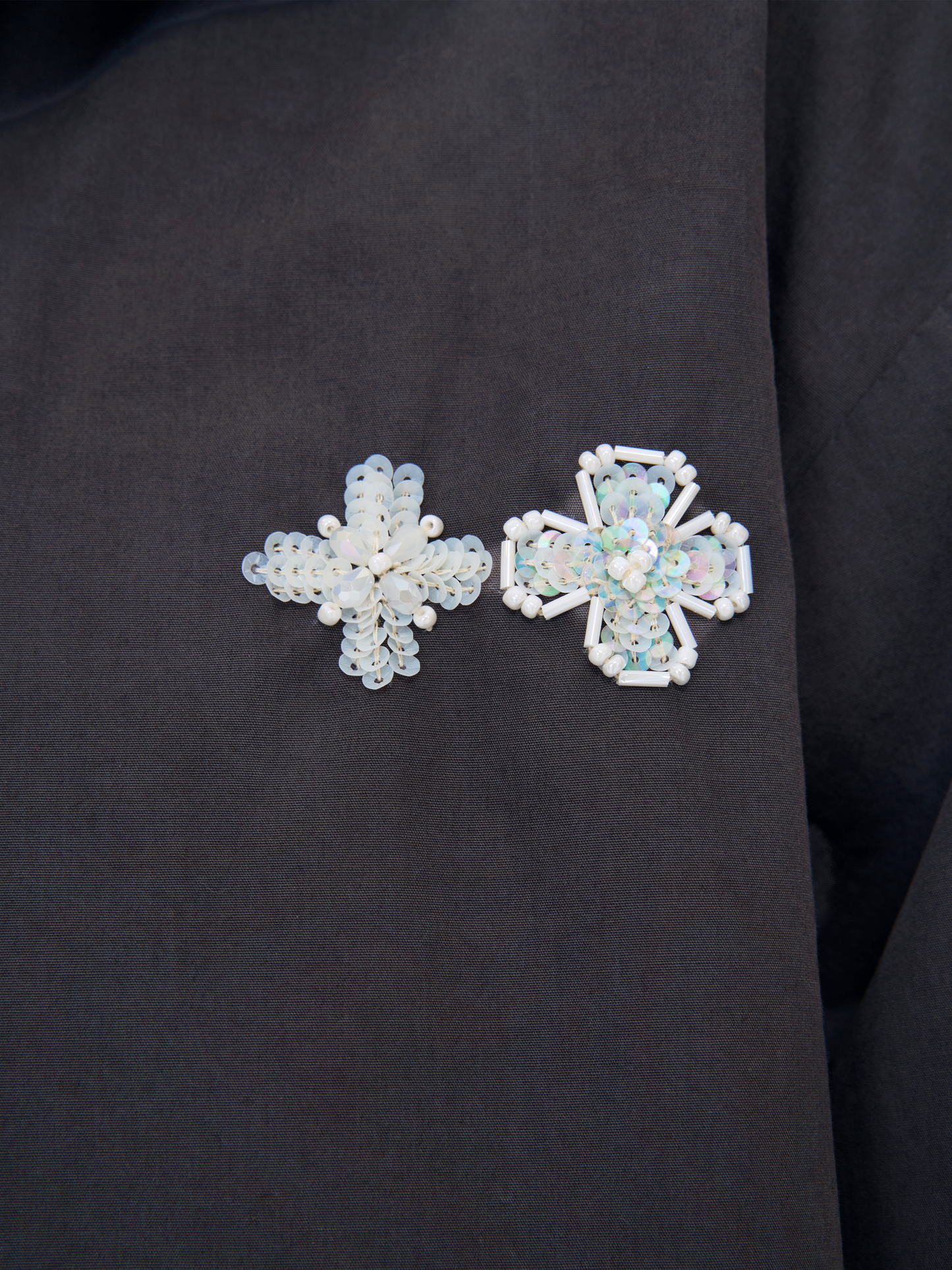 Two beaded brooches, one snowflake-shaped and one cross-shaped, both featuring iridescent white beads on a black fabric background.