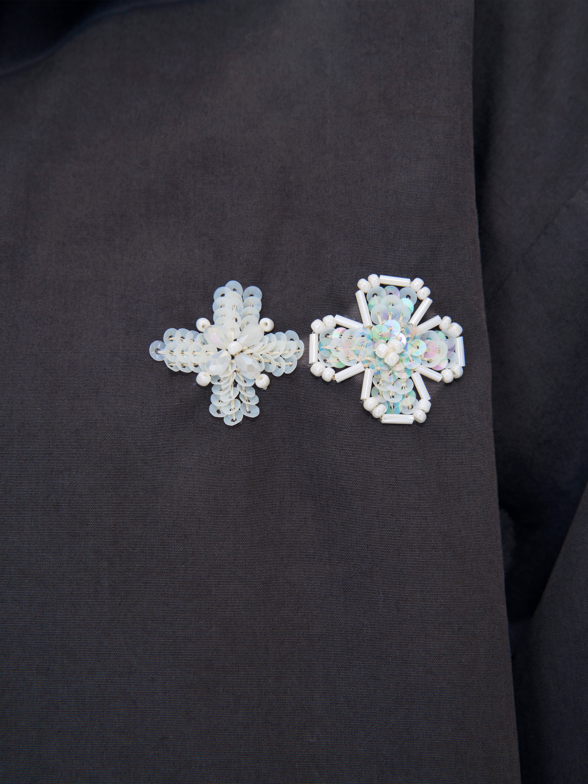 Two beaded brooches, one snowflake-shaped and one cross-shaped, both featuring iridescent white beads on a black fabric background.