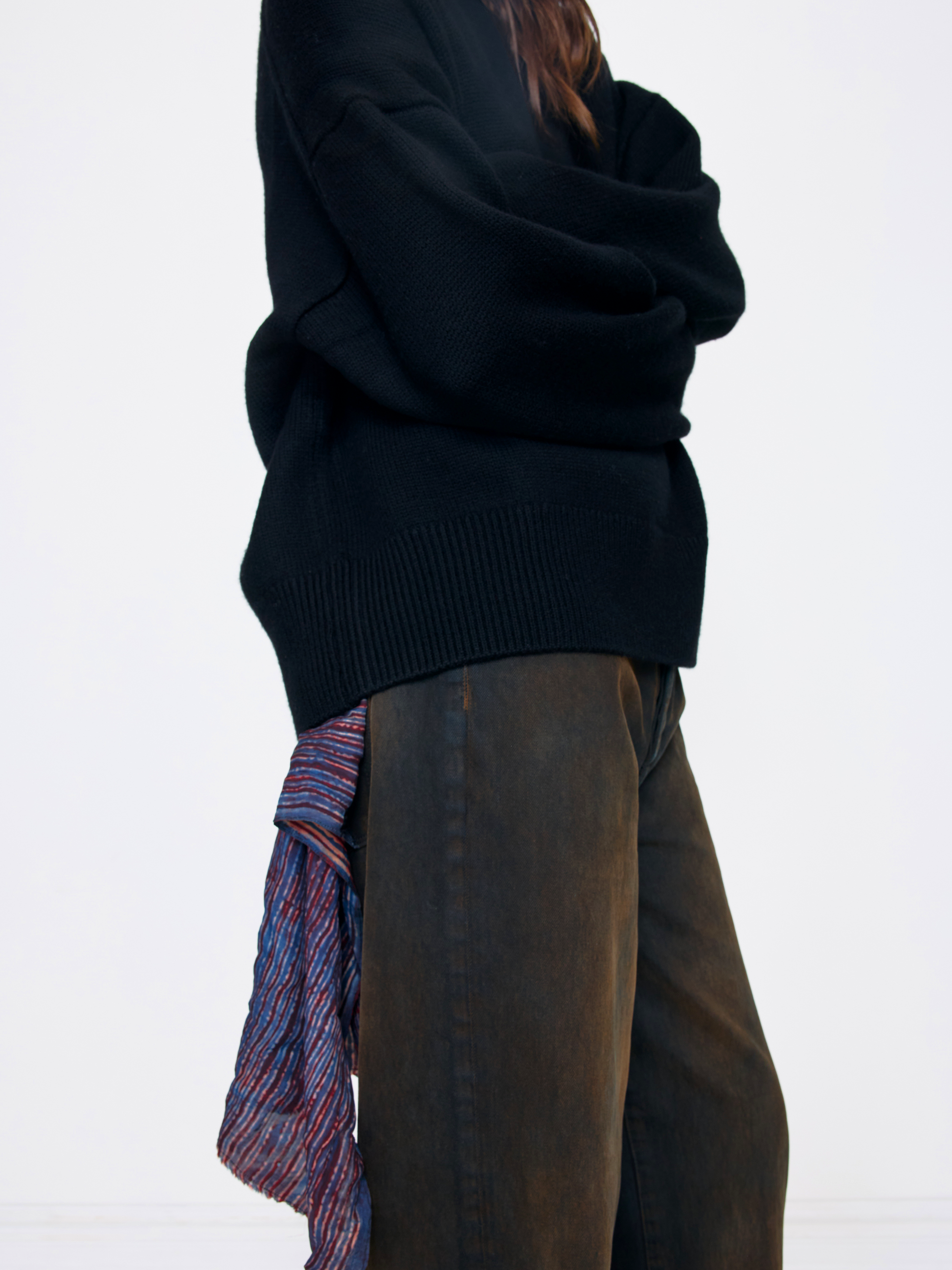 A person shown from the side wearing an oversized black knit sweater, dark brown wide-leg pants, and a striped scarf in blue, red, and white.