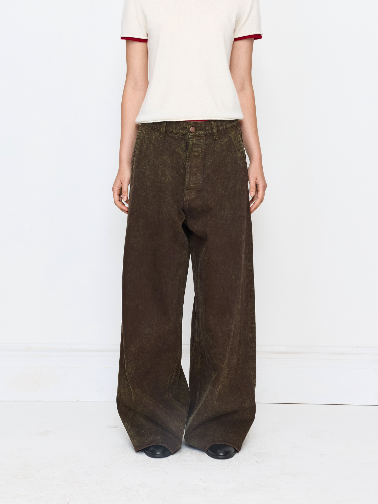 A model is shown from the chest down wearing dark brown wide-leg corduroy pants, a cream t-shirt with red trim, and black shoes against a white studio background.