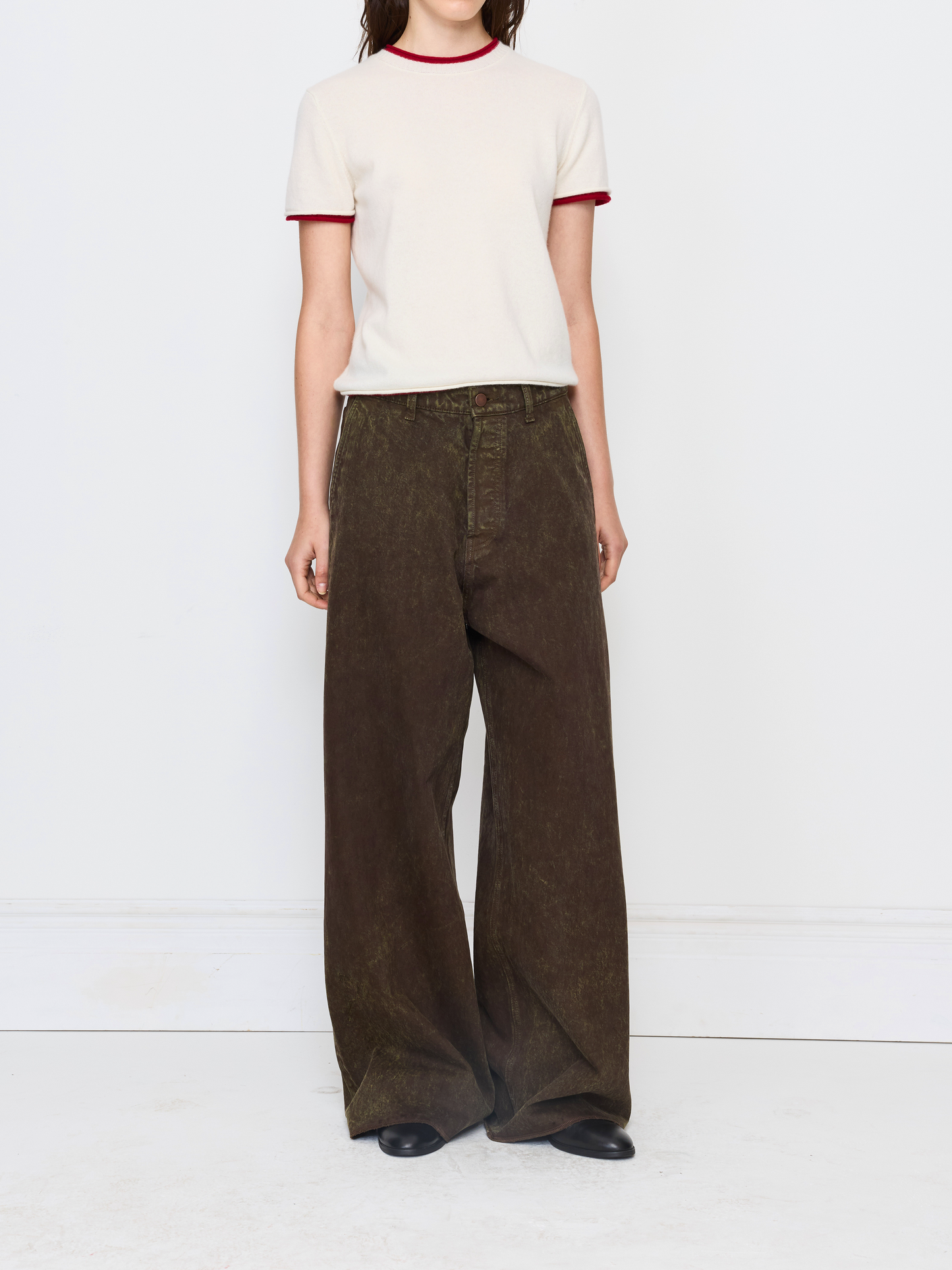 A model wearing a cream ringer t-shirt with red trim and wide-leg brown corduroy pants, standing against a white studio background.