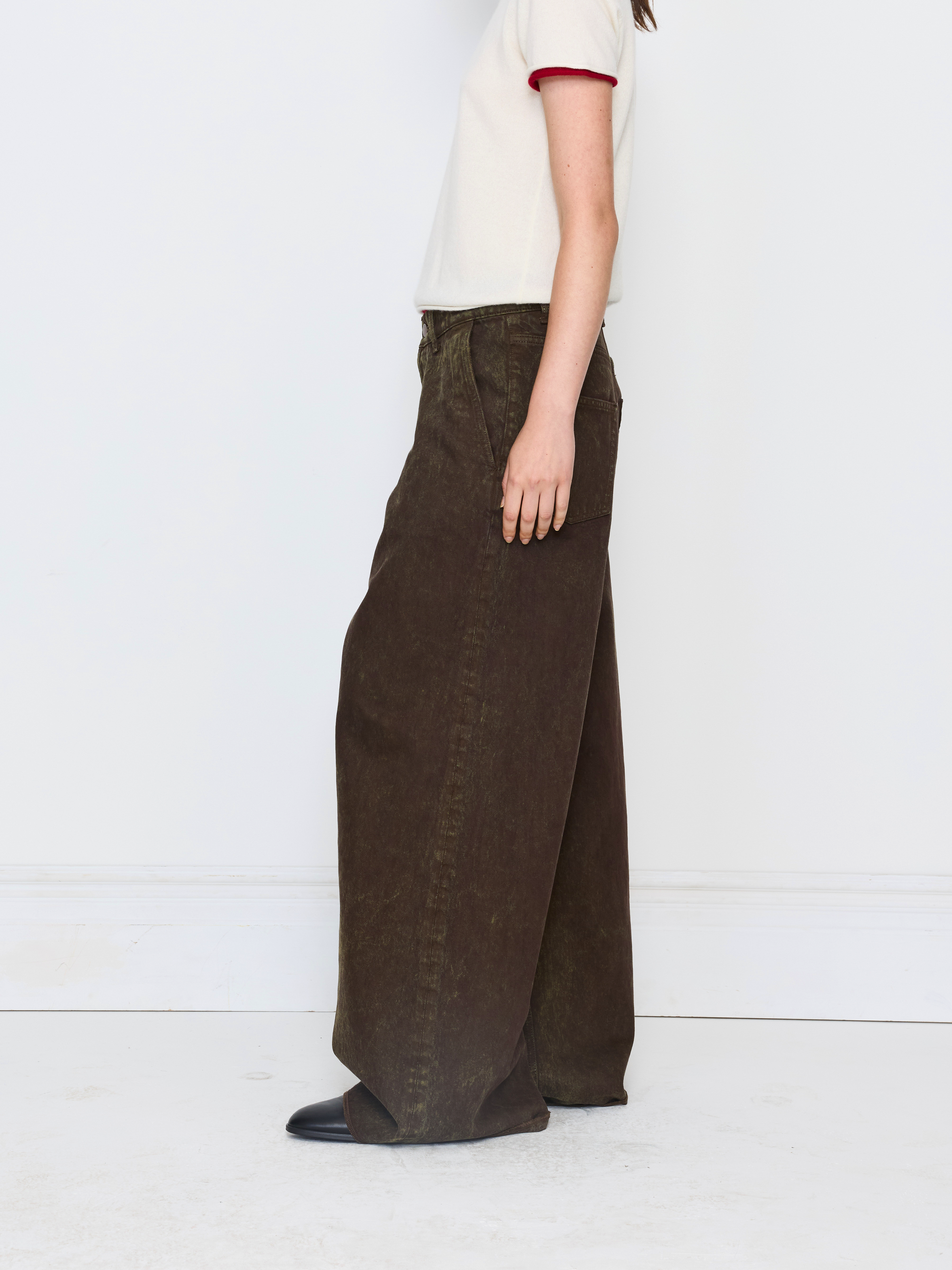 A model shown from the side wearing dark brown wide-leg corduroy pants, a cream ringer t-shirt with red trim, and black shoes, standing against a white studio background.
