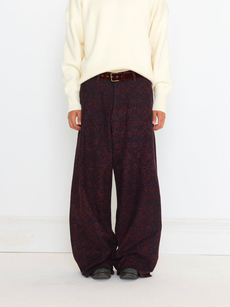 Person wearing a cream sweater and dark patterned pants on a white background
