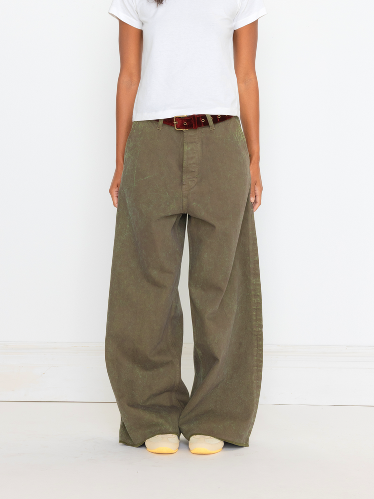 Person wearing olive green wide-leg pants with a white shirt and white shoes on a light gray background