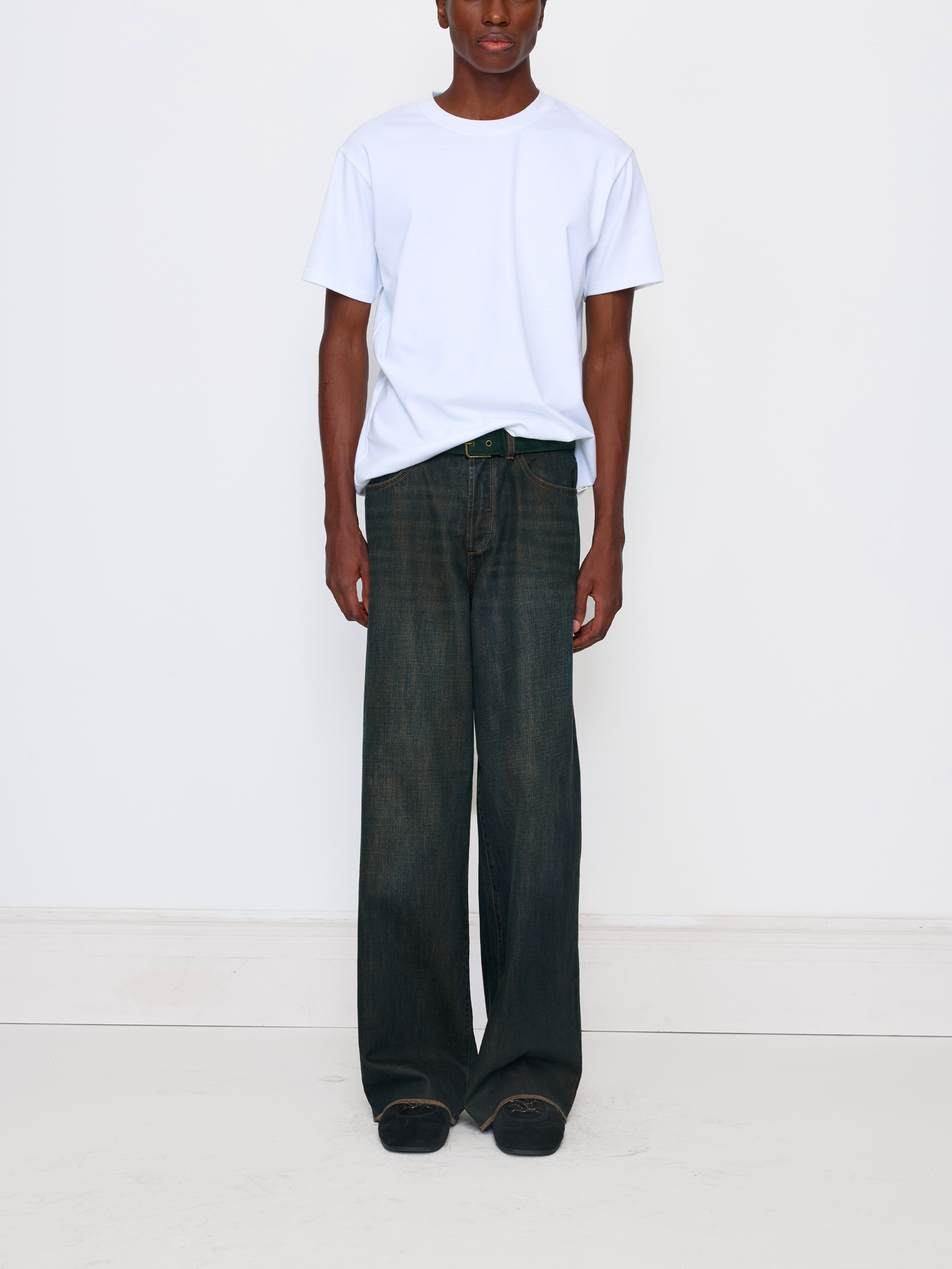 A model wearing a white crewneck t-shirt and dark wide-leg jeans, standing against a plain white studio background.