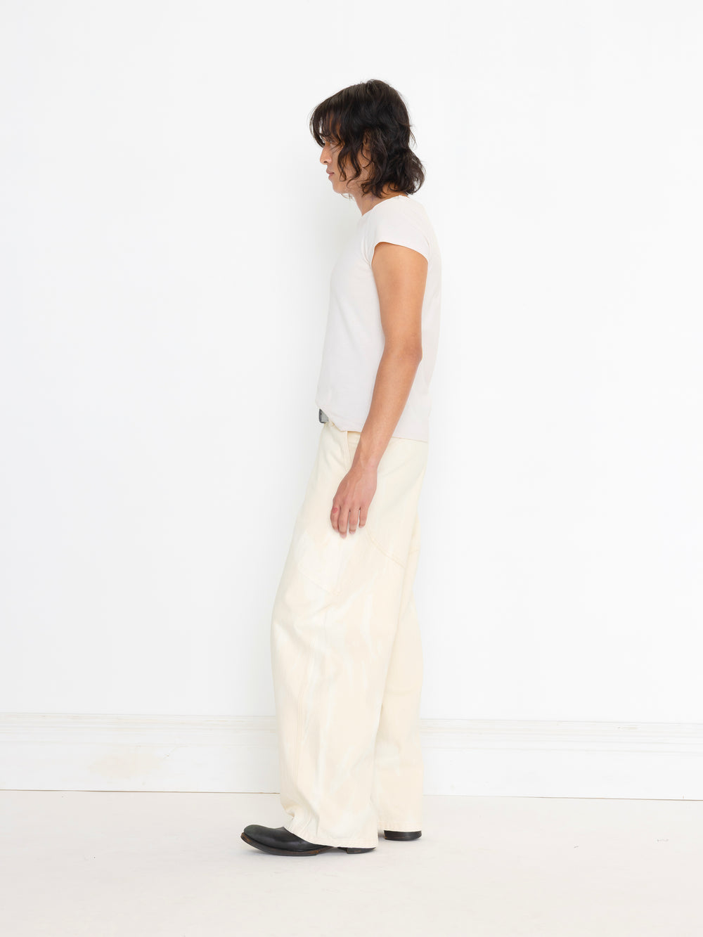 Person wearing a white sleeveless top and cream pants on a white background