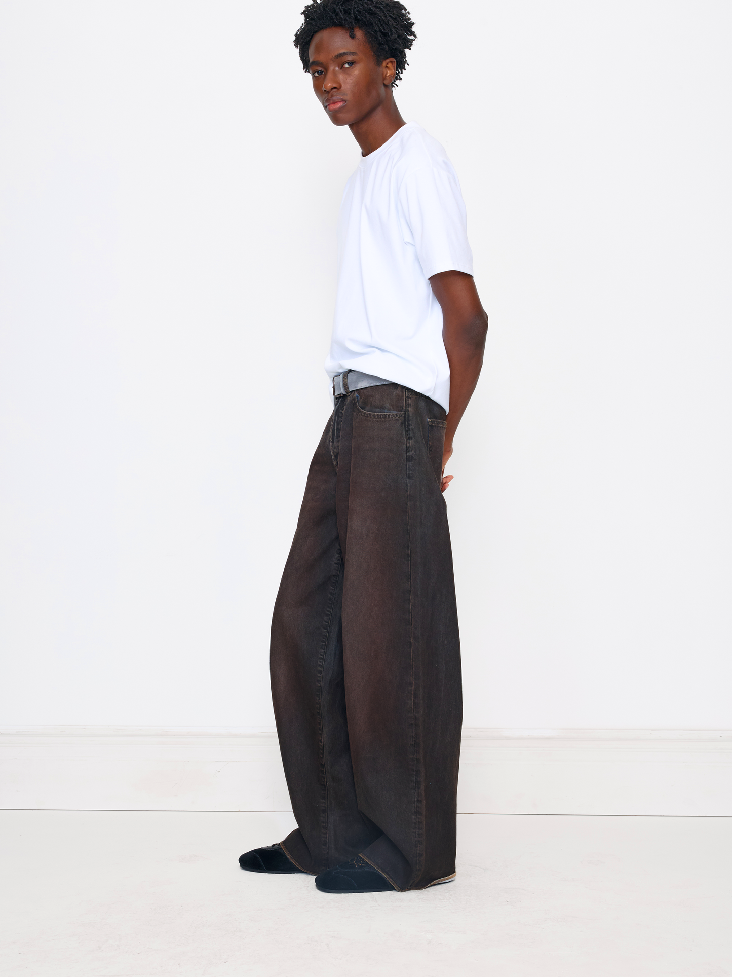 A model wearing a white crewneck t-shirt and dark brown wide-leg denim jeans, standing in profile against a clean white studio background.