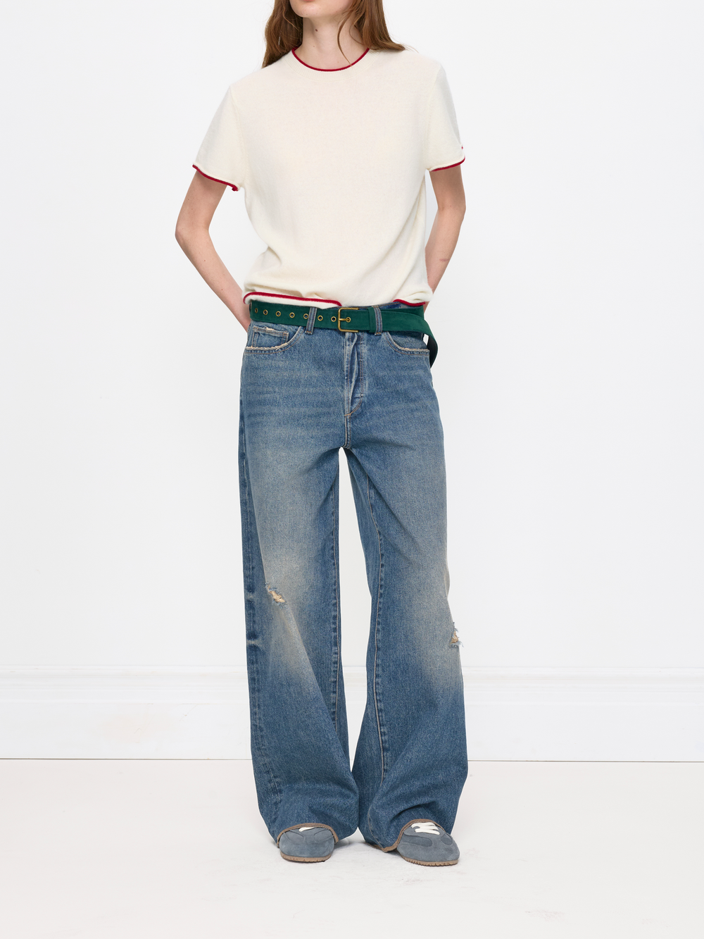 Person wearing a white t-shirt and blue jeans with a green belt on a white background