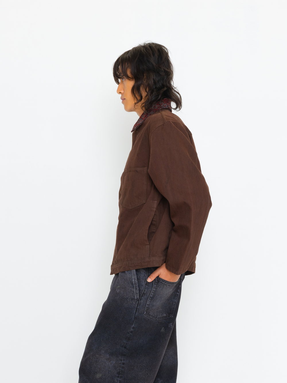 Person wearing a brown jacket and dark jeans against a white background