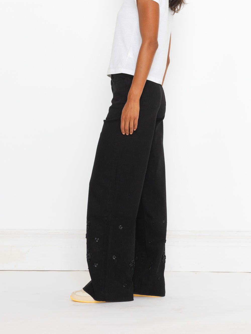 Person wearing black wide-leg pants with button details on a white background