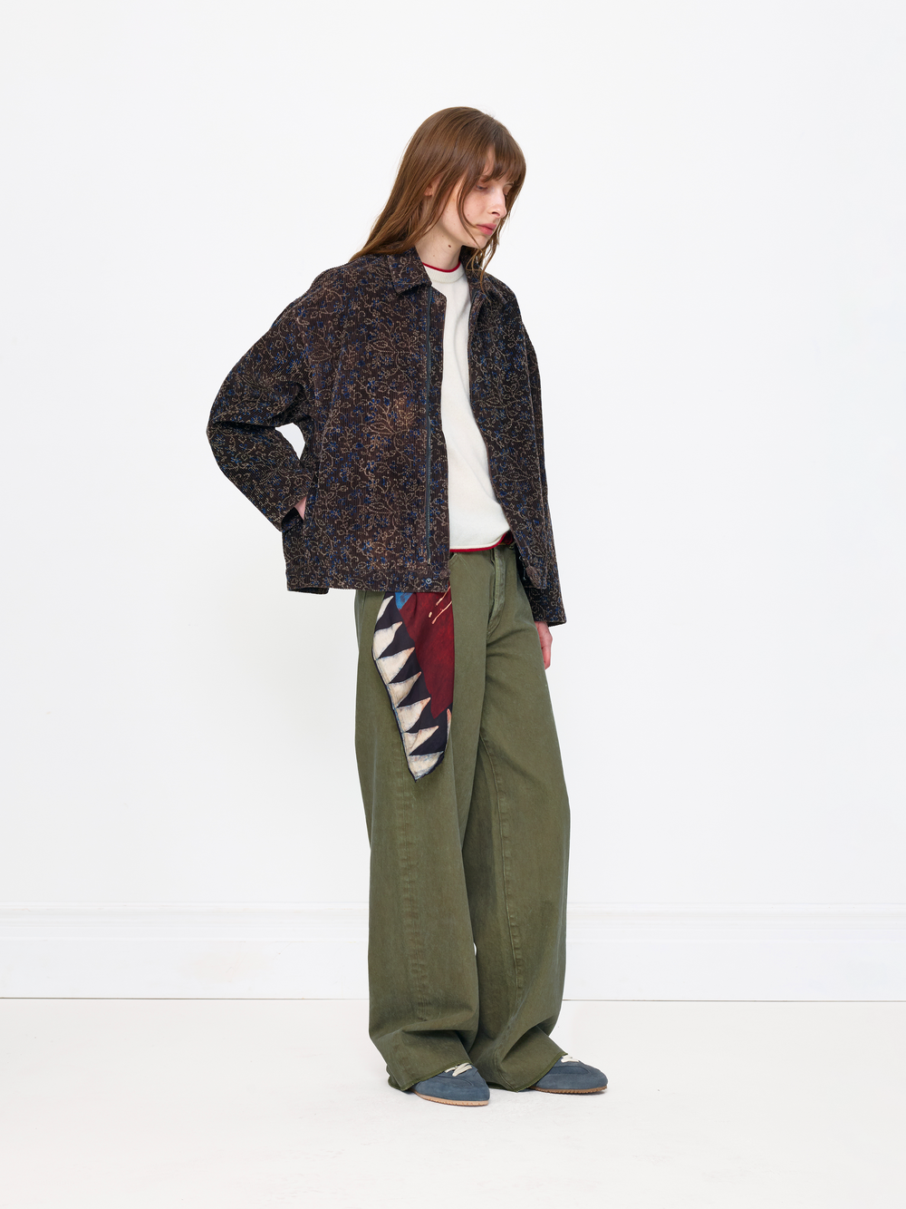 Person wearing a patterned jacket, white shirt, green pants, and blue shoes on a white background